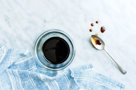 Glass jar of Just Date syrup with a spoon and blue striped cloth on a marble surface.