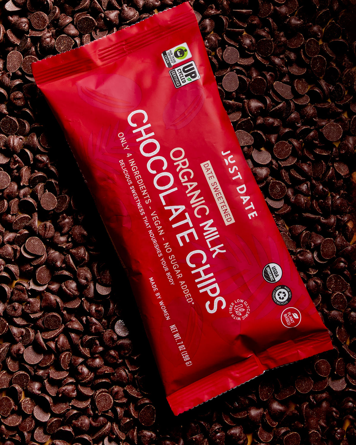 Red package of Just Date Organic Milk Chocolate Chips on a bed of chocolate chips